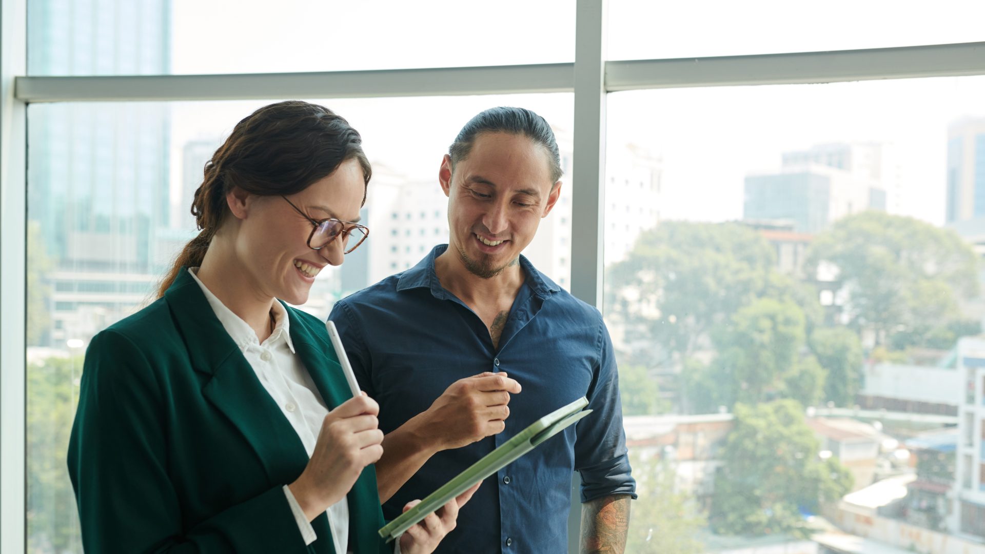 Two colleagues talking by a window with a city view