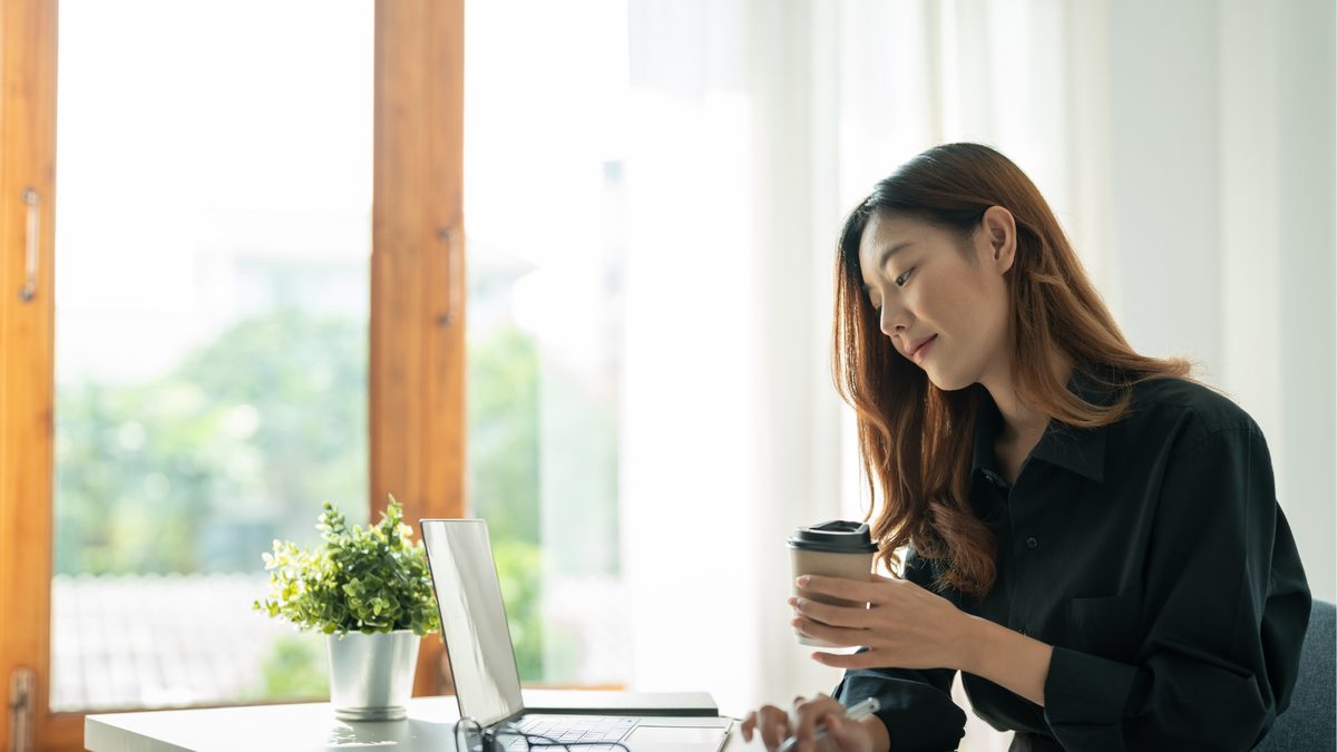 A professional working on a laptop with a coffee by a bright window