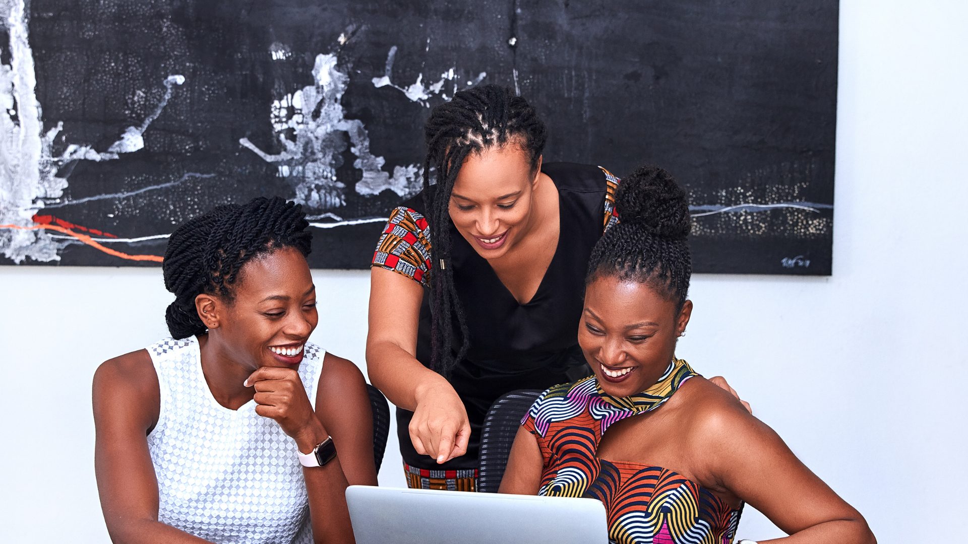 Three colleagues laughing together at a laptop